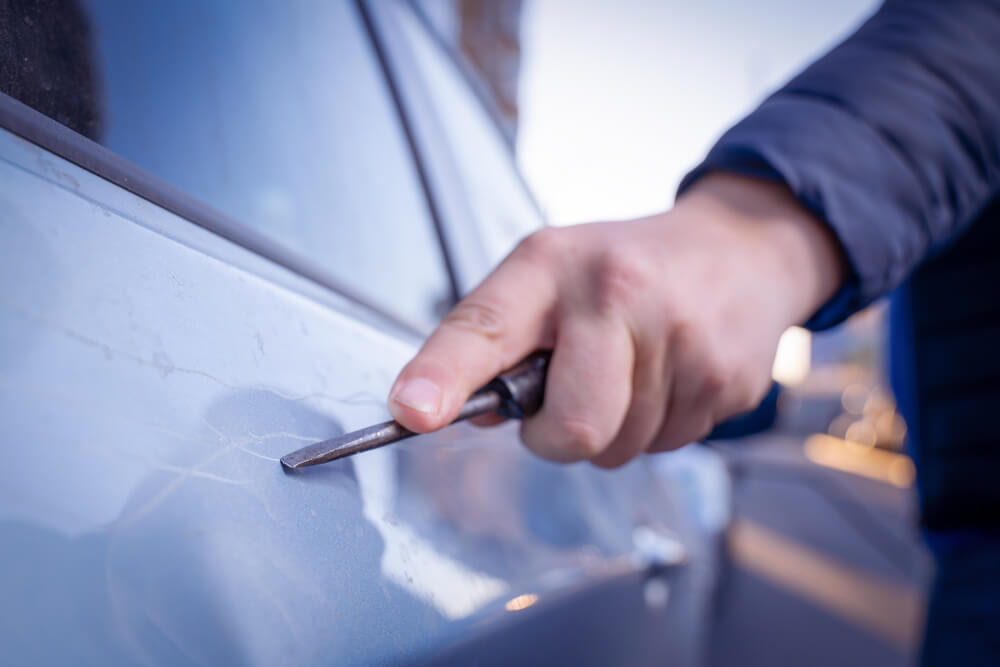 Does Car Insurance Cover Vandalism? An image of a man vandalizing a car by scratching it with a tool.