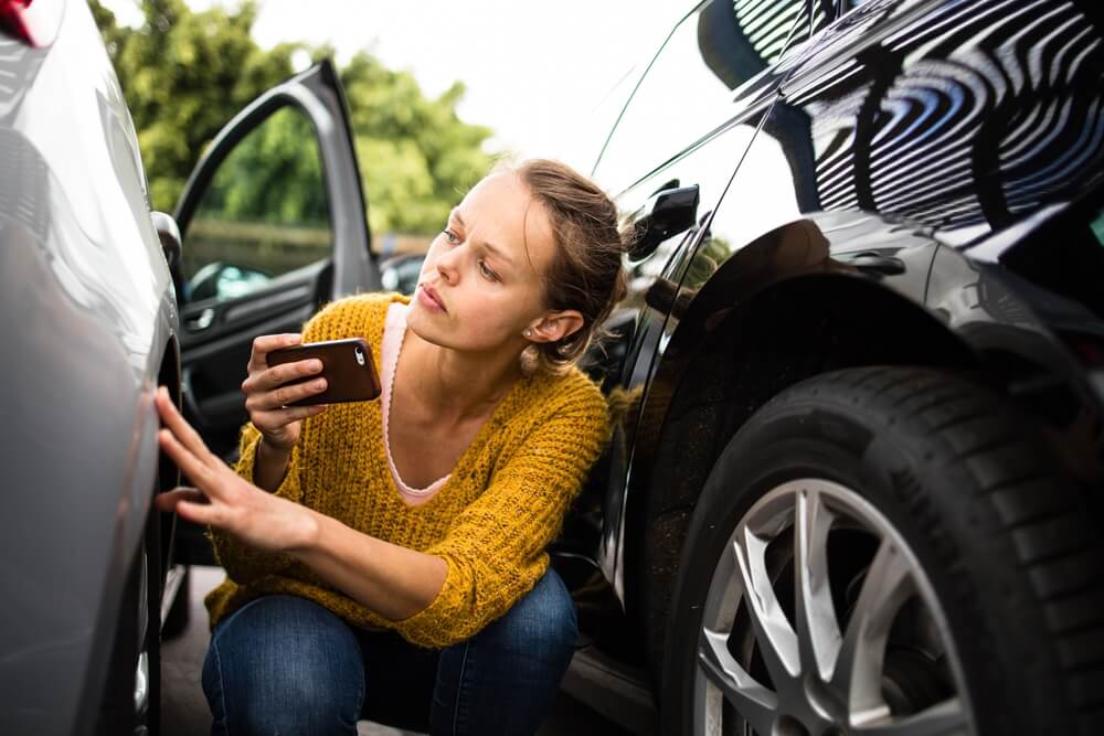 Liability vs Collision Coverage - an image of a woman checking her car after an accident.