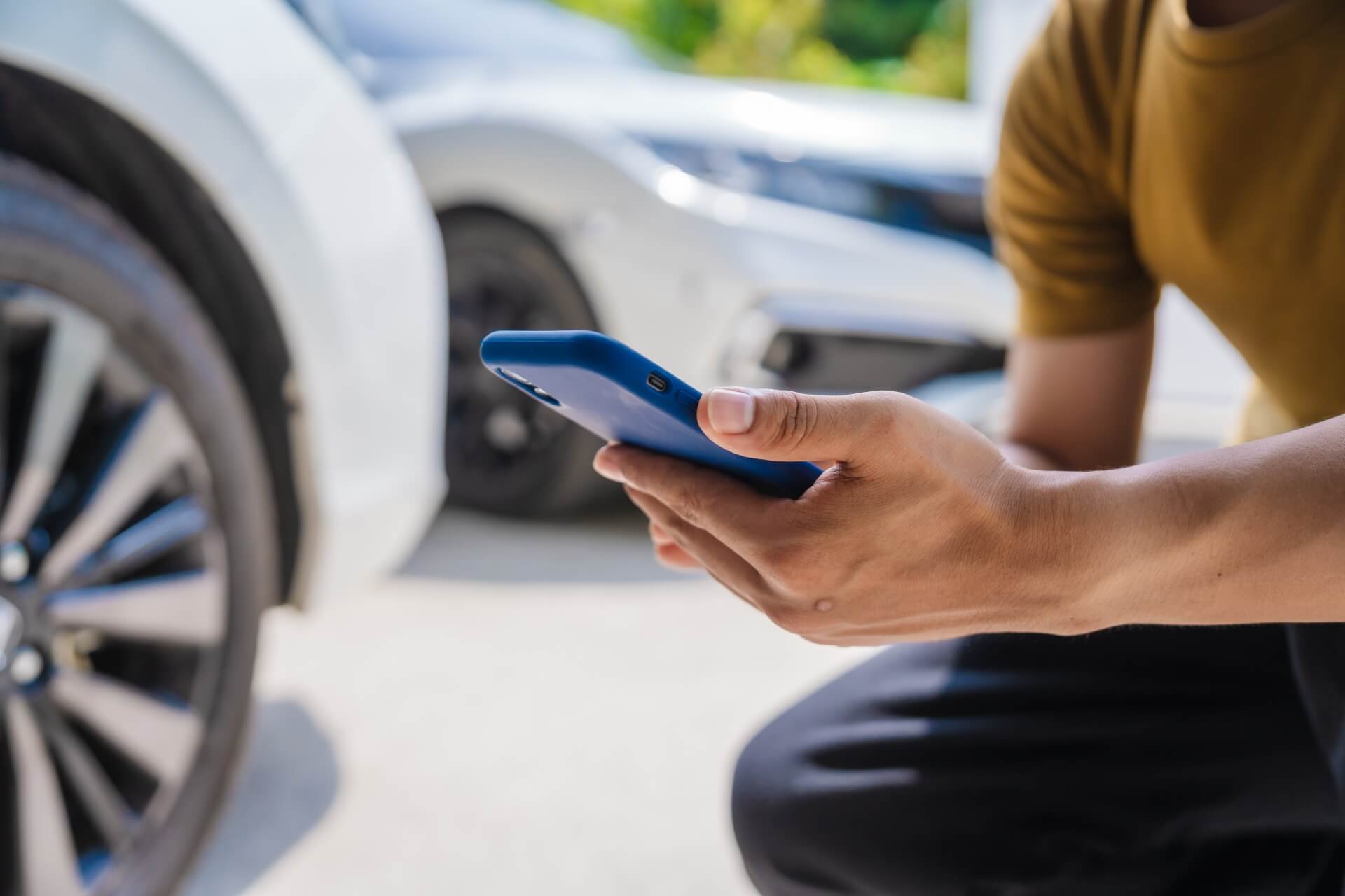 A man looking on his phone, next to a car, about car insurance questions and answers.