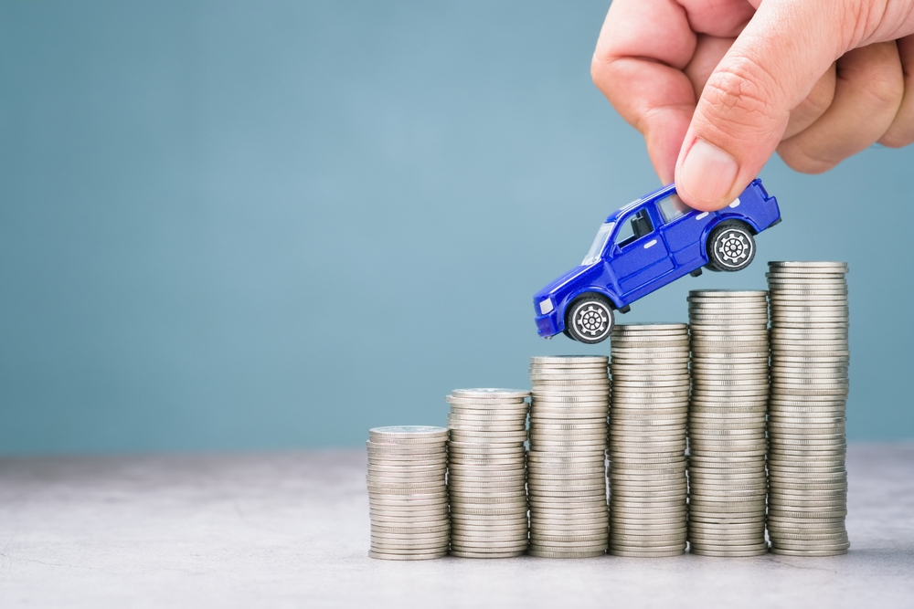 Curious how to lower car insurance? - An image of a car "driving down" a stack of coins.