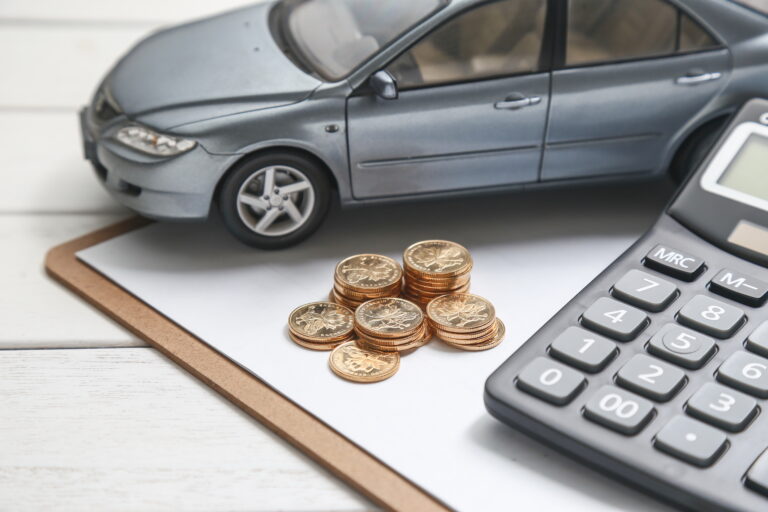 Model car, calculator, and coin stacks on a desk calculating low cost auto insurance rates