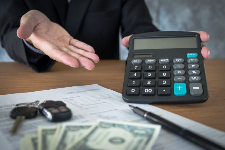 Car dealership representative holding keys and calculating pricing for a vehicle purchase