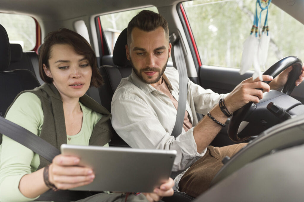 Young couple reviewing digital auto insurance policy options on a tablet inside a car