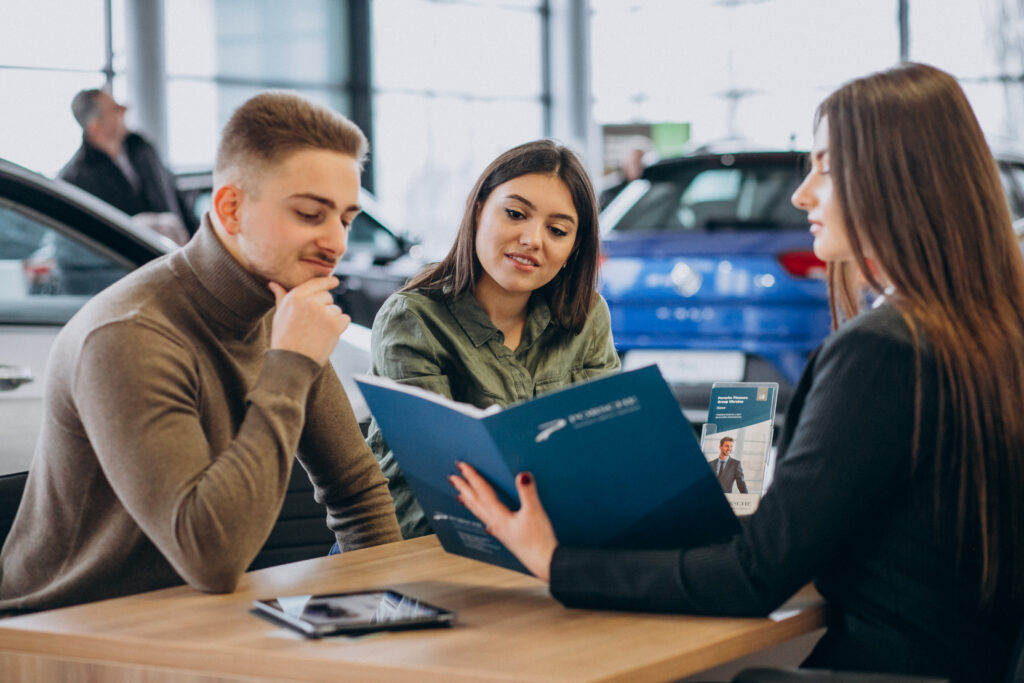 Young couple discussing auto financing and insurance coverage options in a dealership showroom